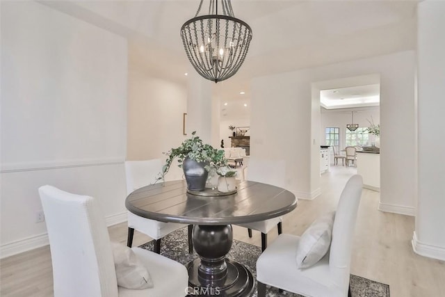 dining space with a chandelier, light hardwood / wood-style floors, and a raised ceiling