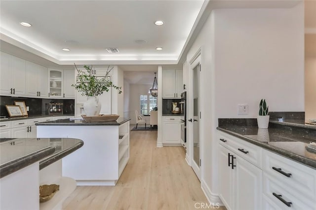 kitchen featuring backsplash, light hardwood / wood-style flooring, a raised ceiling, and white cabinets