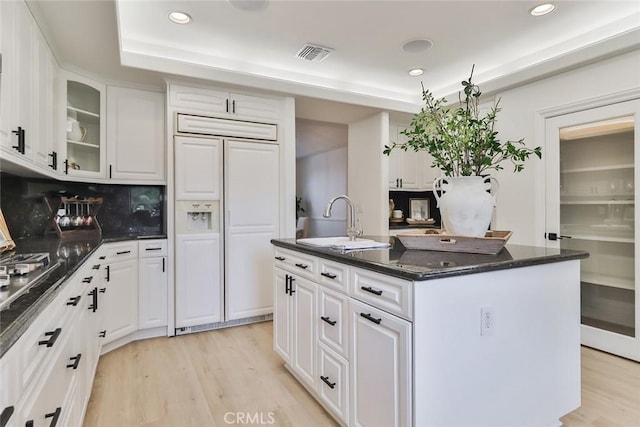 kitchen with sink, paneled built in fridge, a kitchen island with sink, and white cabinets