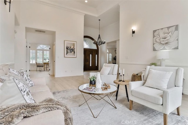 living room with a towering ceiling, a chandelier, and light wood-type flooring