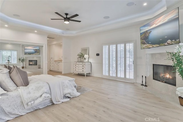 bedroom featuring multiple windows, a tray ceiling, a premium fireplace, and light hardwood / wood-style flooring