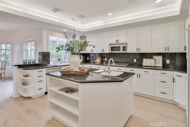 kitchen featuring a raised ceiling, white cabinetry, an island with sink, and light wood-type flooring