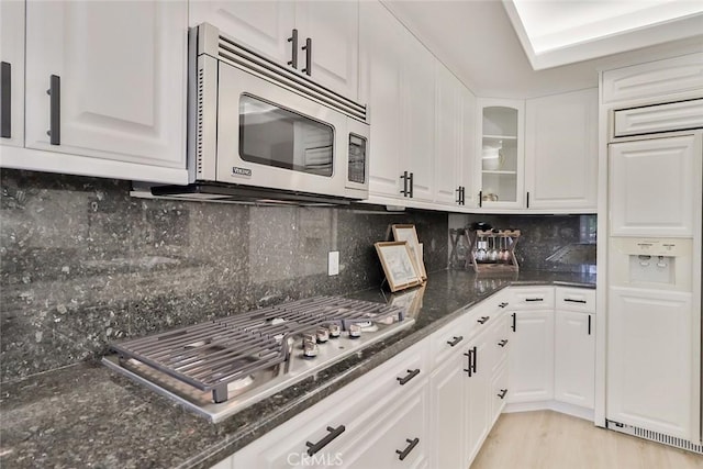 kitchen featuring stainless steel appliances, white cabinetry, tasteful backsplash, and dark stone countertops