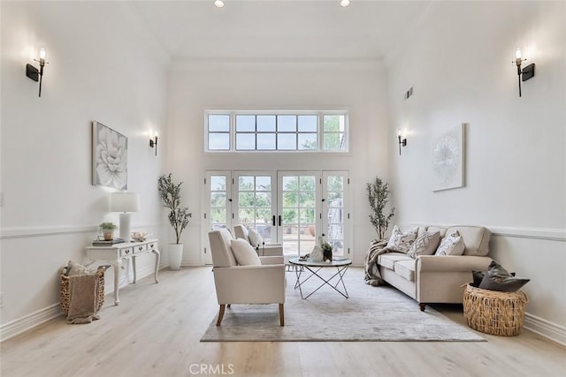 living room with french doors, ornamental molding, a towering ceiling, and light hardwood / wood-style flooring