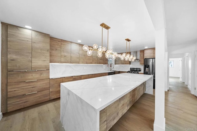 kitchen featuring sink, range, stainless steel refrigerator with ice dispenser, light wood-type flooring, and a spacious island