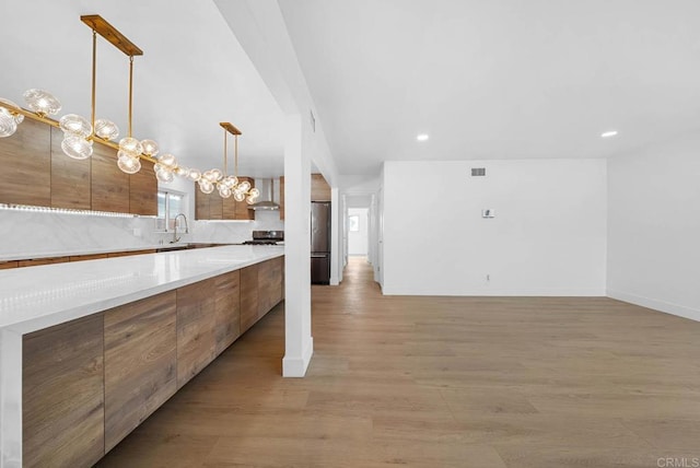 kitchen with stainless steel refrigerator, hanging light fixtures, range, wall chimney exhaust hood, and light hardwood / wood-style flooring