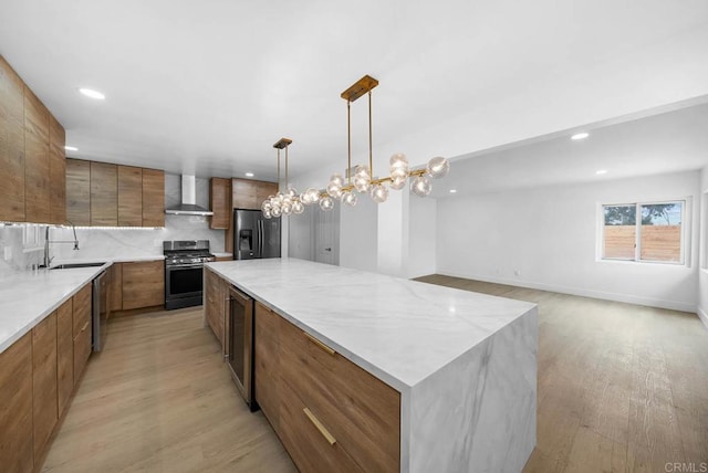 kitchen featuring sink, decorative light fixtures, stainless steel appliances, a large island, and wall chimney range hood