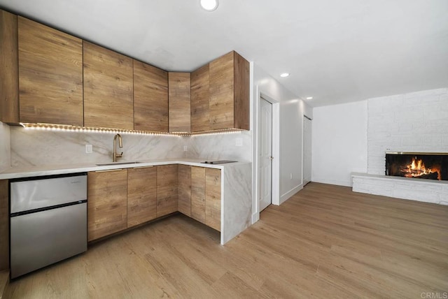 kitchen featuring a stone fireplace, tasteful backsplash, sink, stainless steel fridge, and light hardwood / wood-style flooring