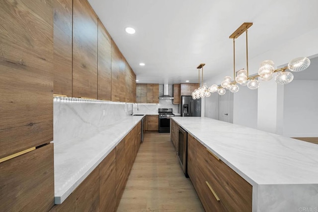 kitchen with a spacious island, sink, hanging light fixtures, stainless steel appliances, and wall chimney exhaust hood