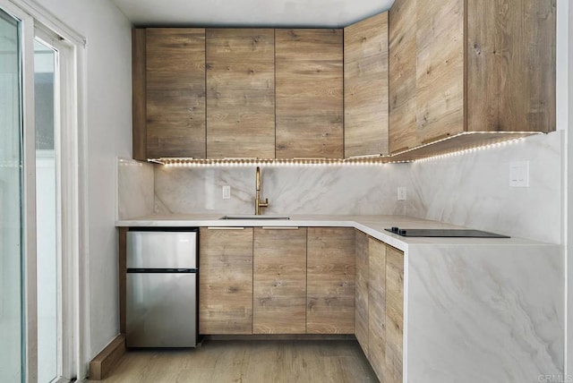 kitchen with sink, stainless steel fridge, decorative backsplash, black electric stovetop, and light hardwood / wood-style flooring