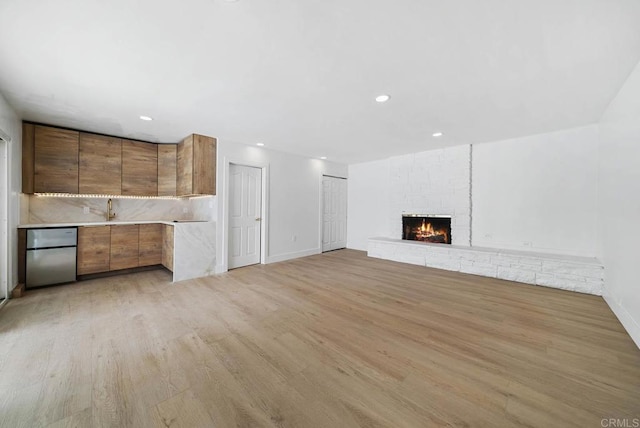 unfurnished living room featuring a fireplace, sink, and light hardwood / wood-style flooring