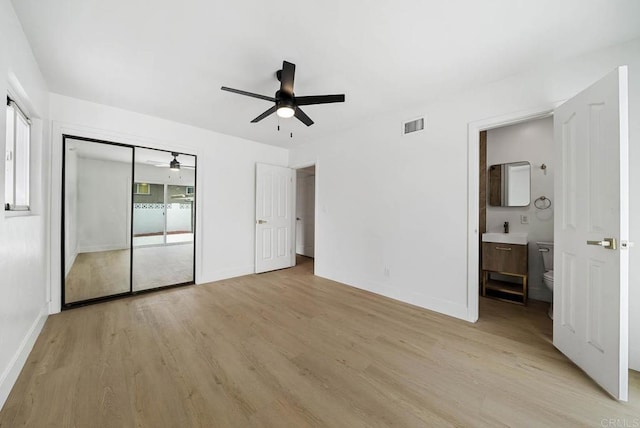 unfurnished bedroom featuring ceiling fan, multiple windows, ensuite bath, and light hardwood / wood-style flooring