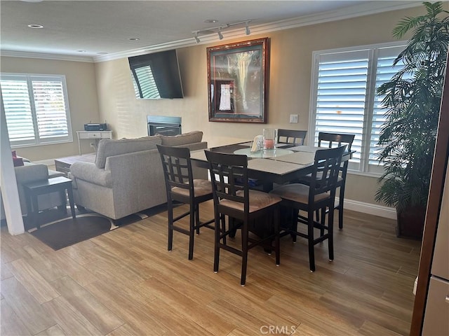 dining area with ornamental molding, rail lighting, and light hardwood / wood-style flooring