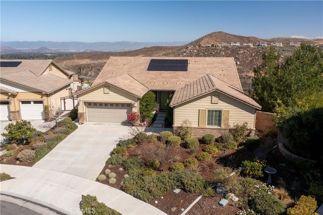 view of front facade with an attached garage, a mountain view, solar panels, a tiled roof, and concrete driveway