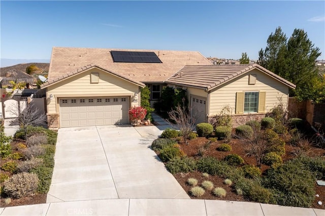 ranch-style house with a garage, concrete driveway, a tile roof, and roof mounted solar panels