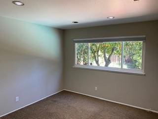 unfurnished room with dark colored carpet and a healthy amount of sunlight