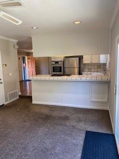 kitchen with white cabinetry, kitchen peninsula, dark carpet, stainless steel appliances, and decorative backsplash