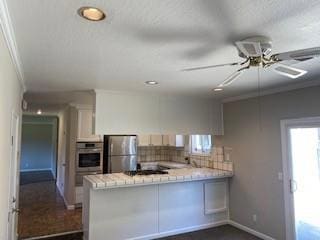 kitchen featuring ceiling fan, appliances with stainless steel finishes, white cabinetry, decorative backsplash, and kitchen peninsula