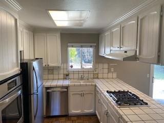 kitchen with dark parquet floors, range hood, white cabinets, tile counters, and stainless steel appliances