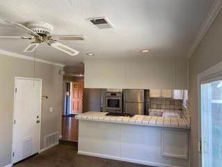 kitchen with ornamental molding, stainless steel appliances, tile countertops, and kitchen peninsula