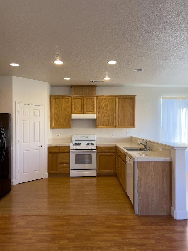 kitchen with sink, wood-type flooring, a textured ceiling, kitchen peninsula, and white appliances