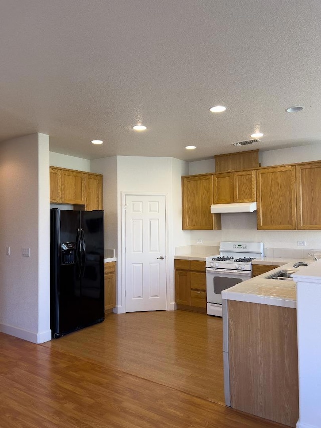 kitchen featuring sink, black fridge, a textured ceiling, dark hardwood / wood-style flooring, and white gas range oven