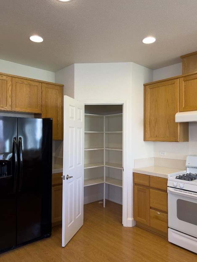 kitchen with black fridge, a textured ceiling, white range with gas stovetop, and light hardwood / wood-style flooring