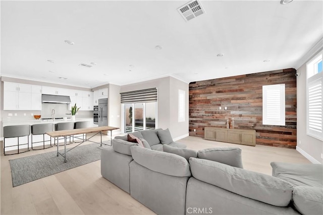 living room with crown molding, wooden walls, sink, and light wood-type flooring