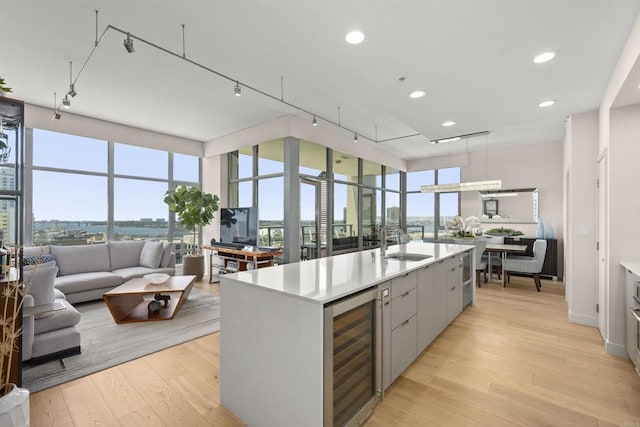 kitchen with sink, beverage cooler, floor to ceiling windows, a center island with sink, and light hardwood / wood-style flooring