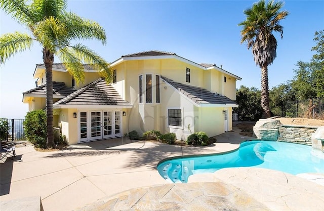 rear view of property featuring a swimming pool with hot tub, french doors, and a patio area