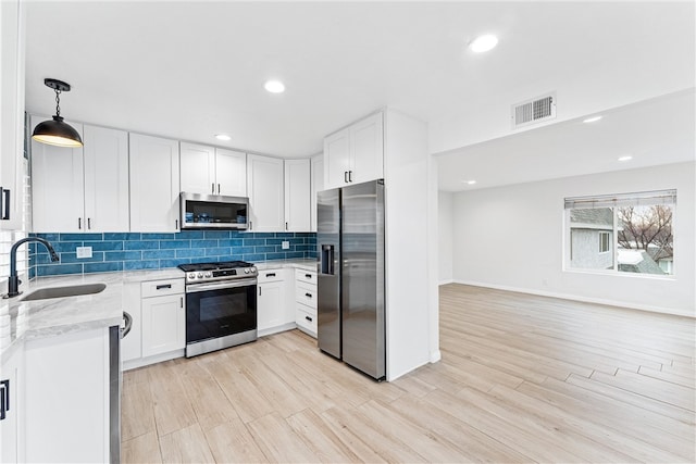 kitchen with sink, light stone counters, decorative light fixtures, stainless steel appliances, and white cabinets