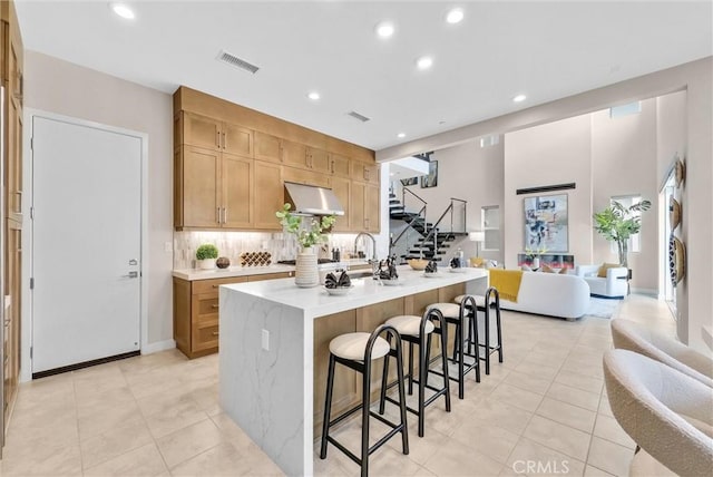 kitchen featuring visible vents, open floor plan, under cabinet range hood, a kitchen bar, and backsplash