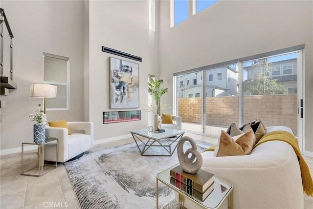 tiled living area featuring a glass covered fireplace, a towering ceiling, and baseboards