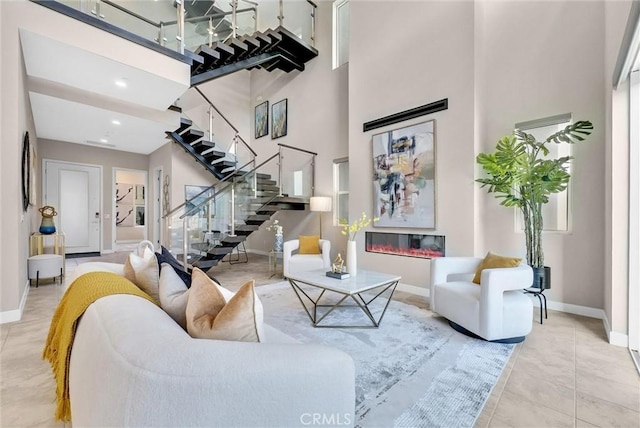 living area with stairs, a high ceiling, baseboards, and a glass covered fireplace