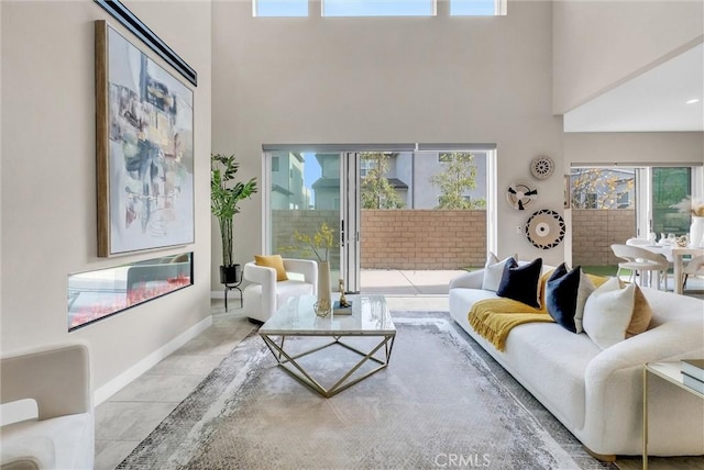 tiled living area featuring a glass covered fireplace, a towering ceiling, and baseboards