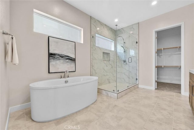 full bathroom with a spacious closet, a soaking tub, a marble finish shower, and baseboards