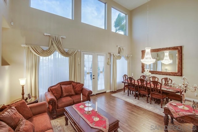 living room with plenty of natural light, a towering ceiling, hardwood / wood-style floors, and french doors