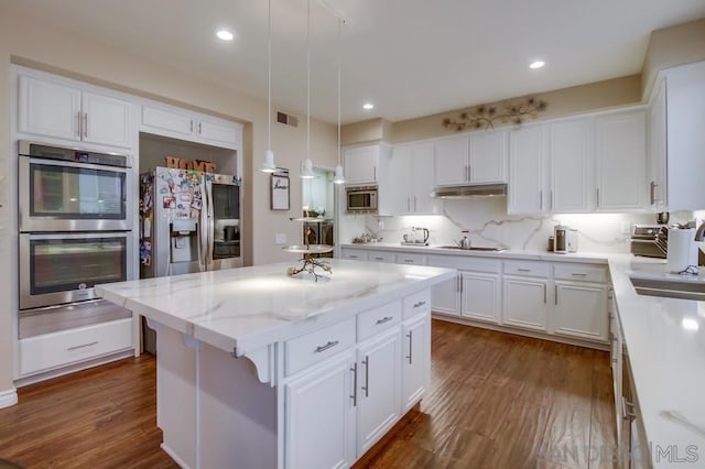 kitchen with appliances with stainless steel finishes, white cabinetry, dark hardwood / wood-style flooring, hanging light fixtures, and a center island