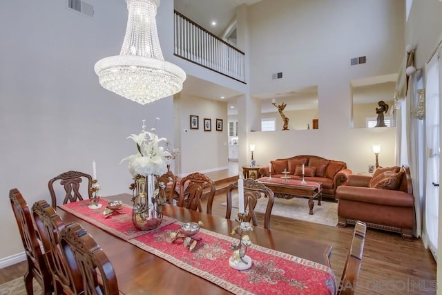 dining area with wood-type flooring, a towering ceiling, and a notable chandelier