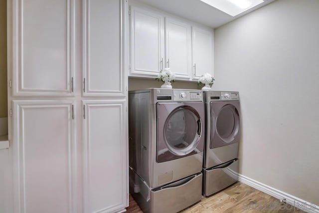 washroom featuring a skylight, cabinets, washing machine and clothes dryer, and light wood-type flooring