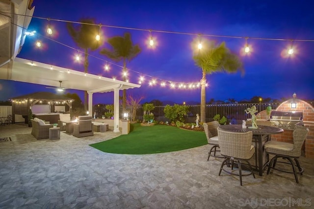 patio at night featuring a grill, an outdoor hangout area, a lawn, and exterior kitchen