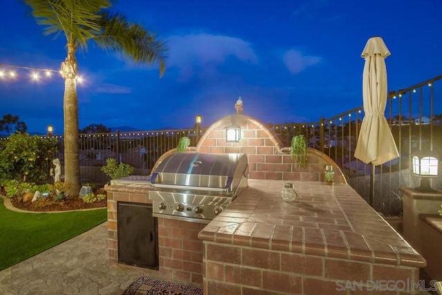 patio at twilight featuring an outdoor kitchen and area for grilling