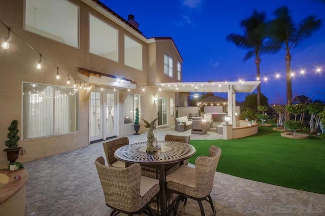 patio at night featuring an outdoor living space, a yard, and french doors