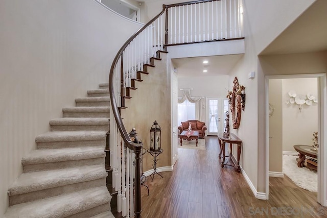 staircase with a towering ceiling and wood-type flooring