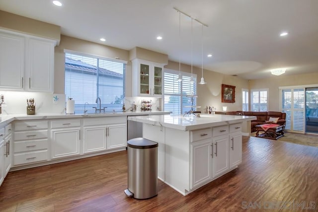 kitchen featuring dark wood-type flooring, sink, decorative light fixtures, a center island, and white cabinets