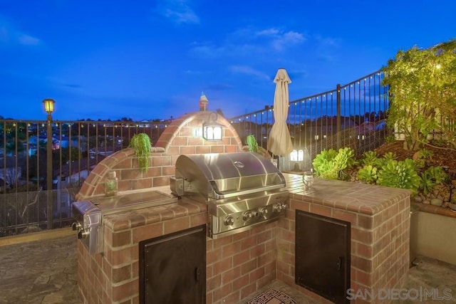 patio terrace at dusk featuring a grill and an outdoor kitchen