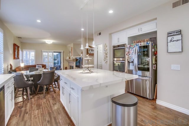 kitchen featuring pendant lighting, appliances with stainless steel finishes, wood-type flooring, white cabinets, and a kitchen island