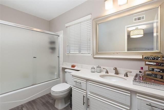 full bath featuring visible vents, bath / shower combo with glass door, toilet, wood finished floors, and vanity