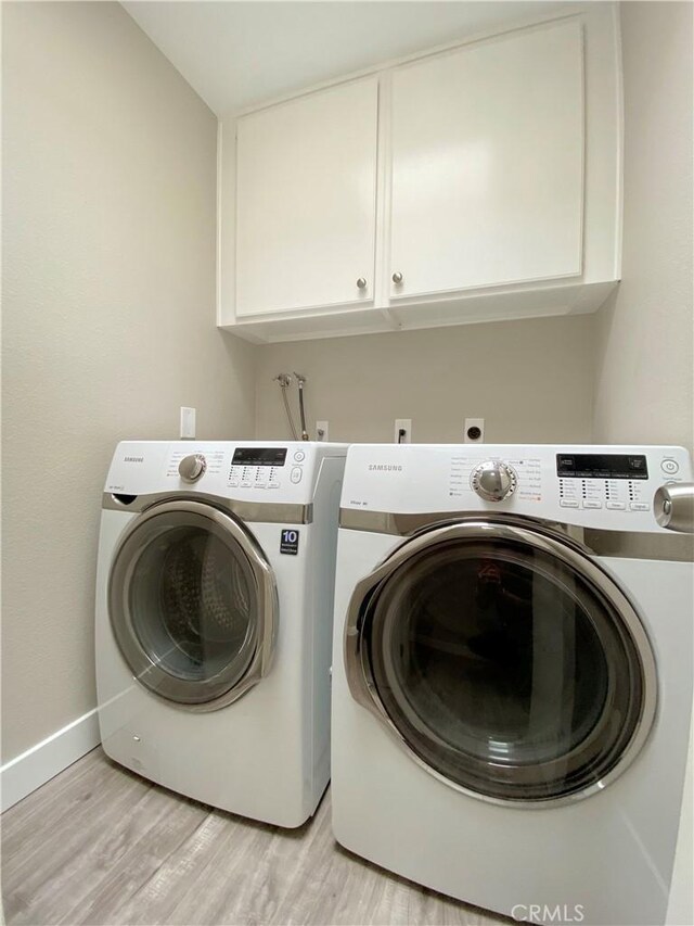 laundry area with light wood finished floors, washer and clothes dryer, cabinet space, and baseboards