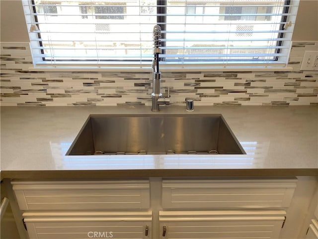 details featuring light countertops, tasteful backsplash, a sink, and white cabinets